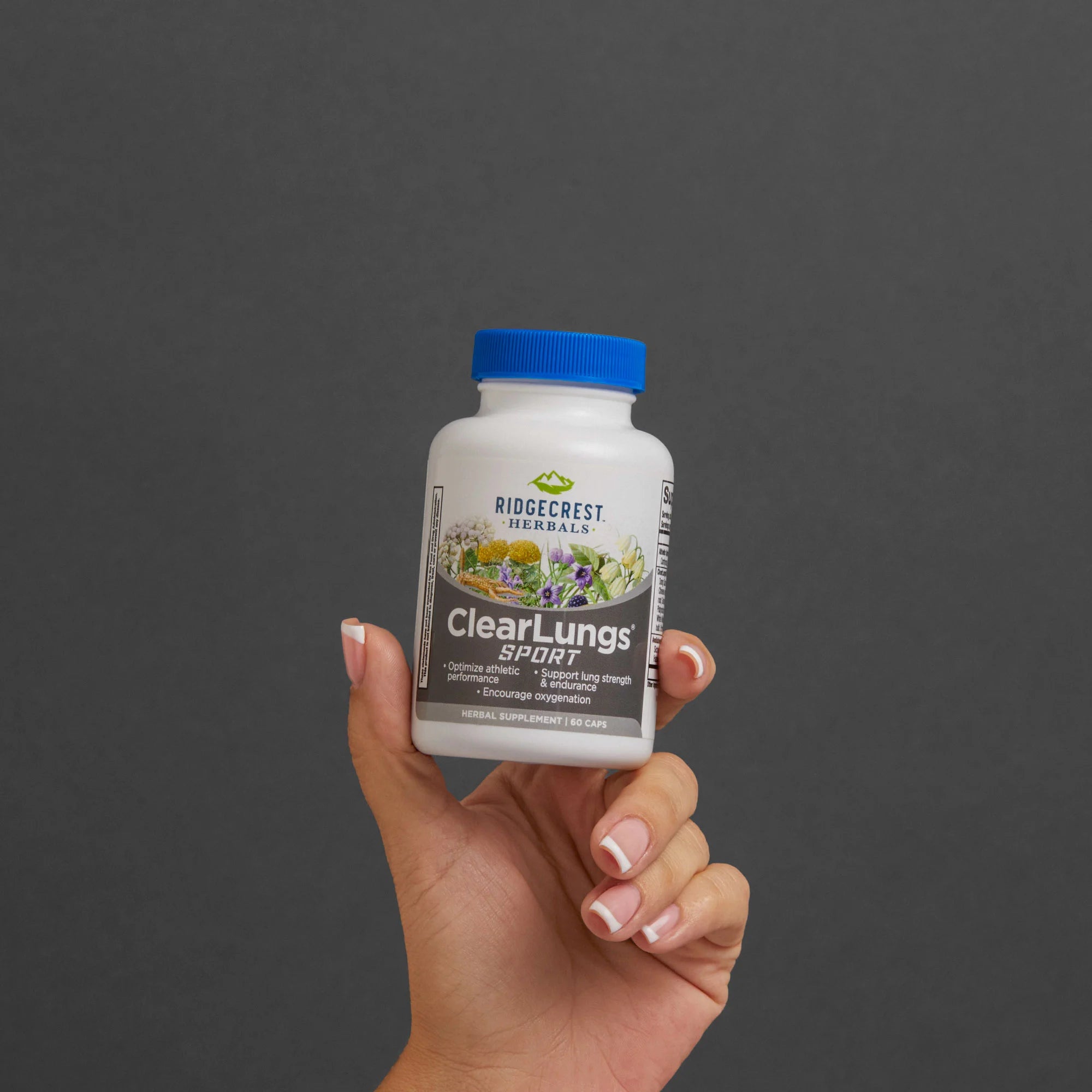 A manicured female hand holds a bottle of ClearLungs Sport against a gray background
