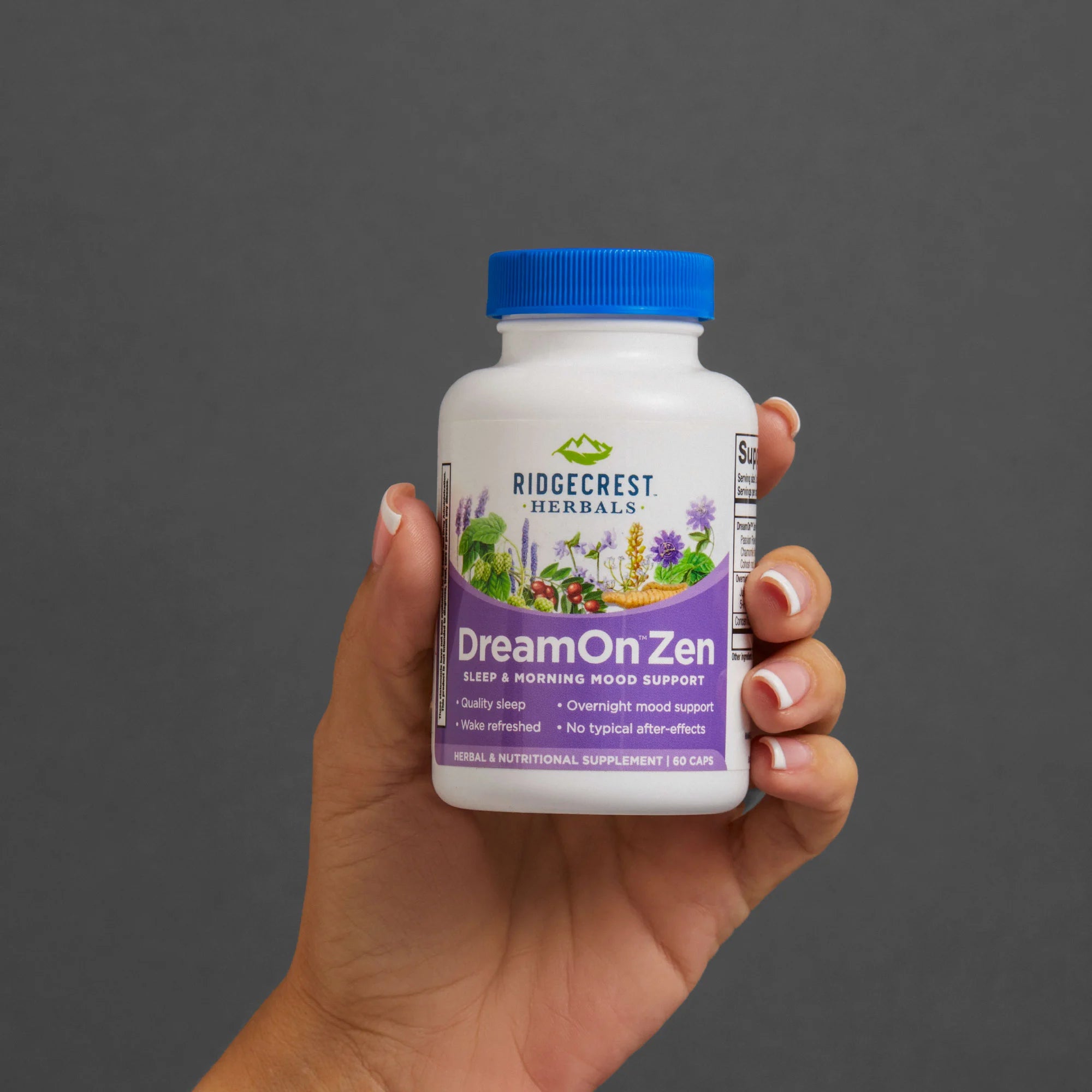 A manicured female hand holds a bottle of DreamOn Zen against a gray background