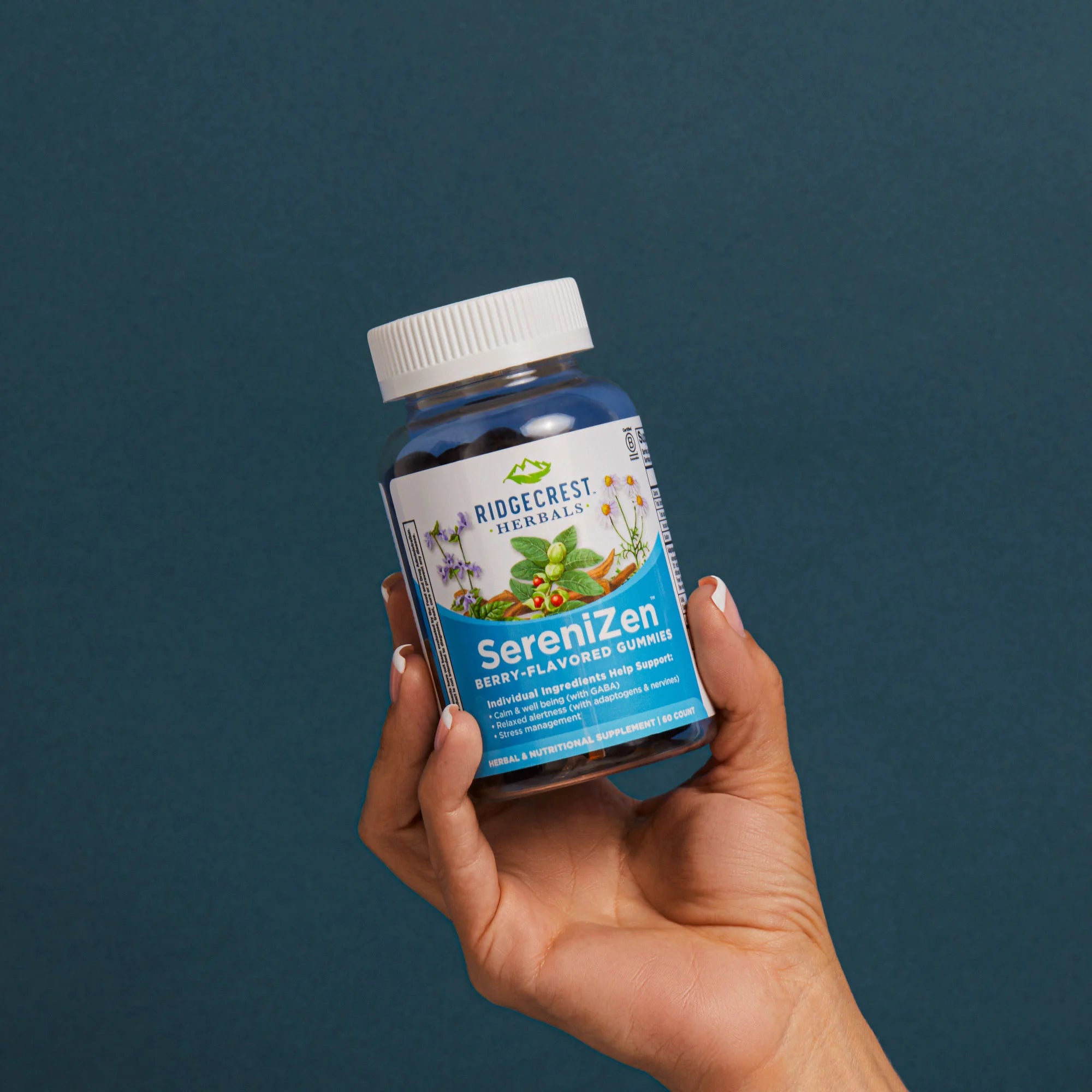 A manicured female hand holds a bottle of SereniZen Gummies against a teal background.