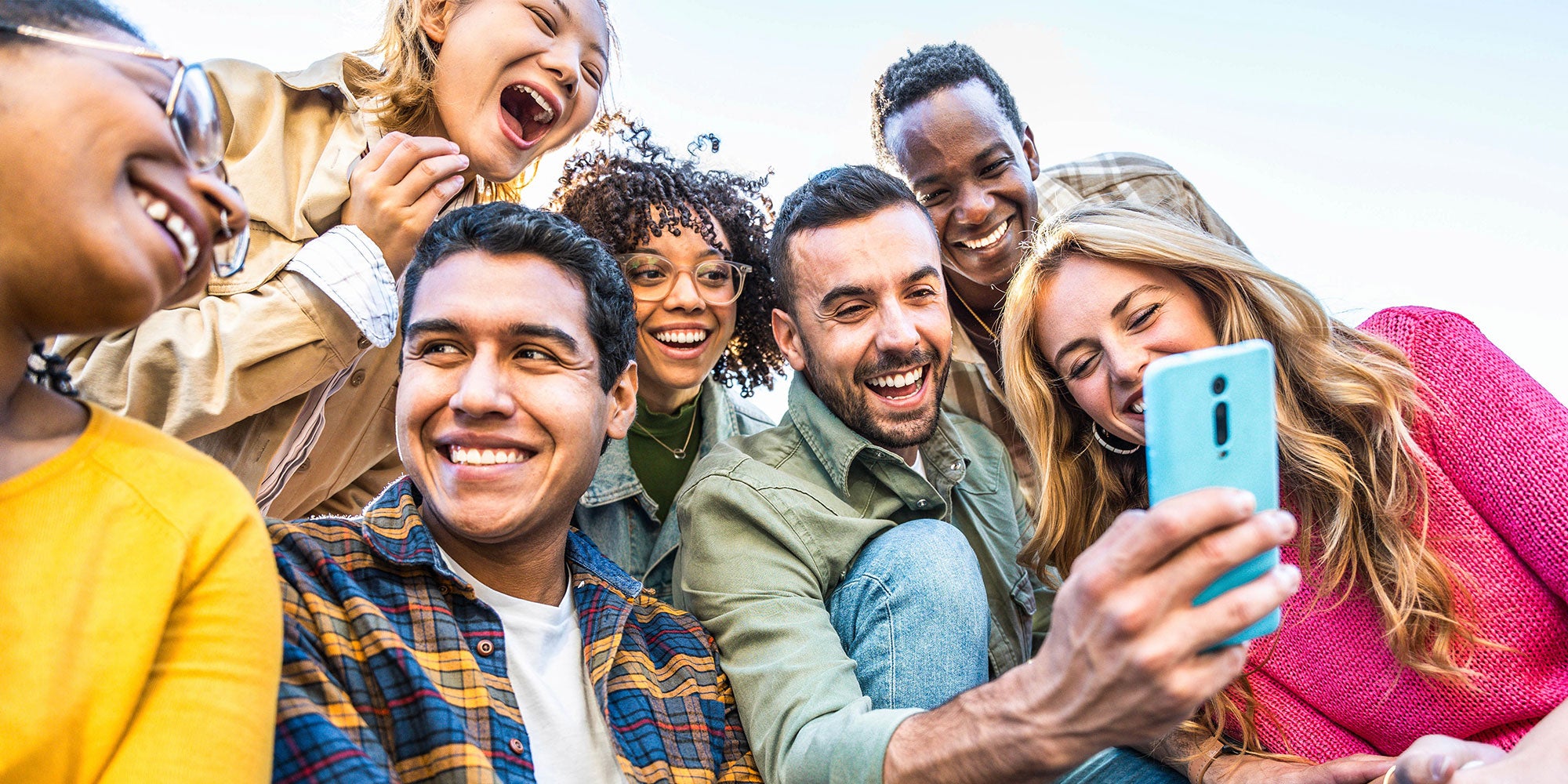 A diverse group of friends happily gathered outdoors, smiling and laughing as they take a selfie together on a sunny day.