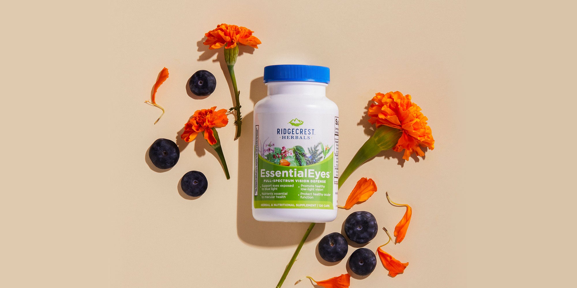 EssentialEyes supplement is displayed with vibrant orange marigold flowers and scattered blueberries, set against a beige background.