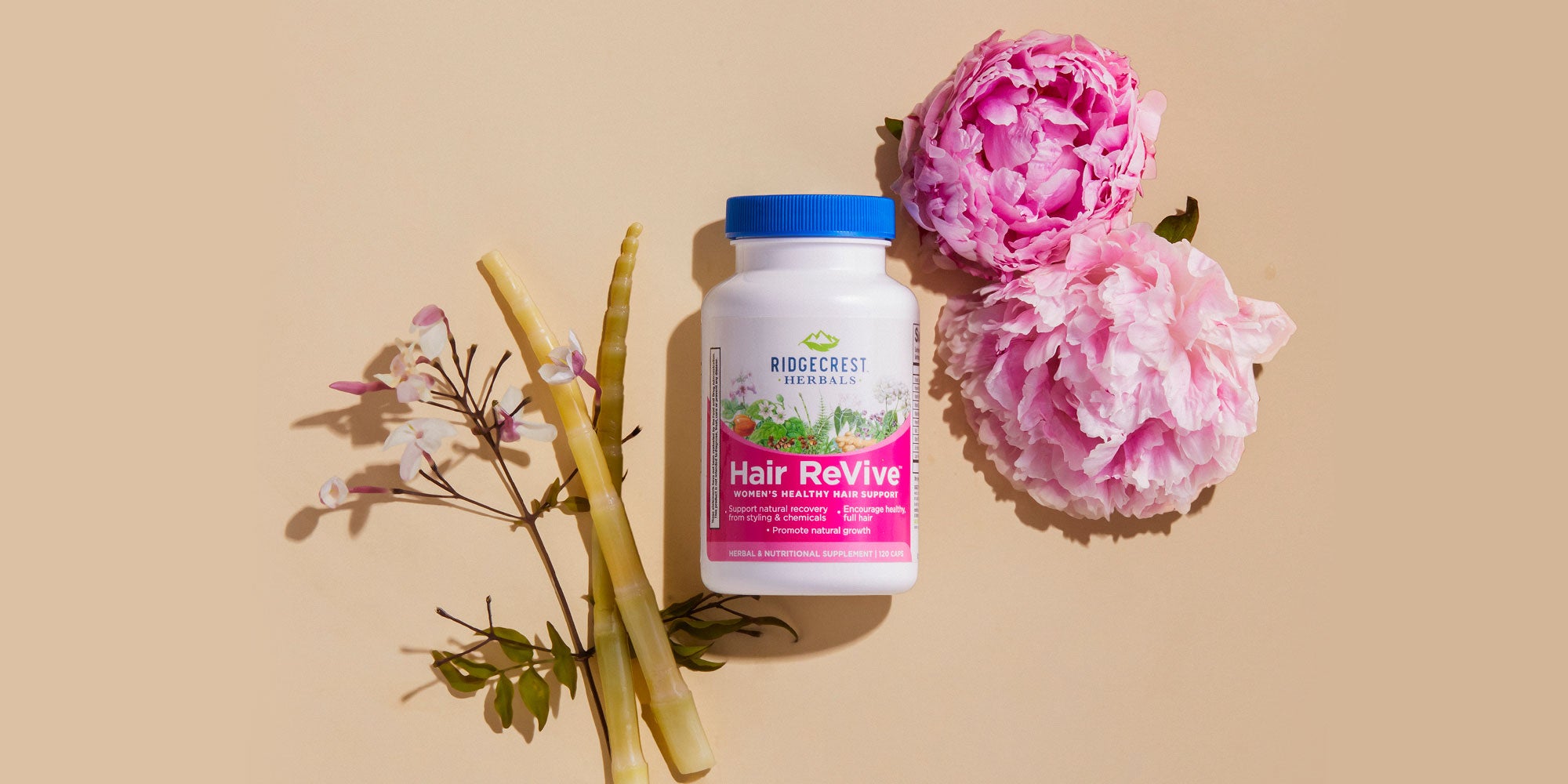 Hair ReVive bottle is displayed with pink peonies, bamboo, and delicate white flowers, set against a beige background.