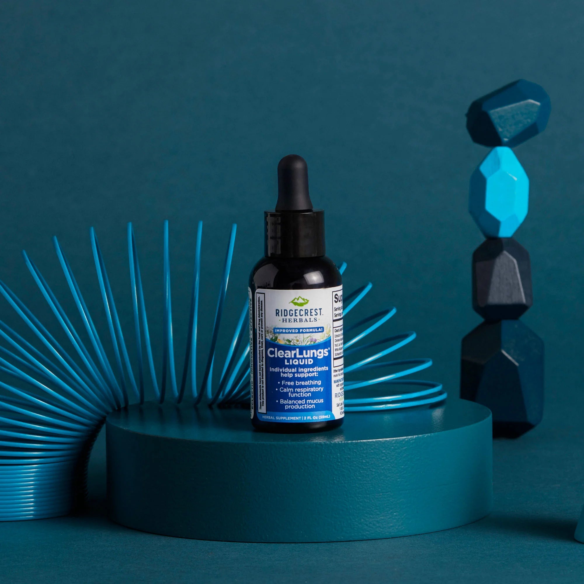 ClearLungs Liquid supplement is displayed with blue geometric shapes and a blue slinky toy, against a dark teal background.