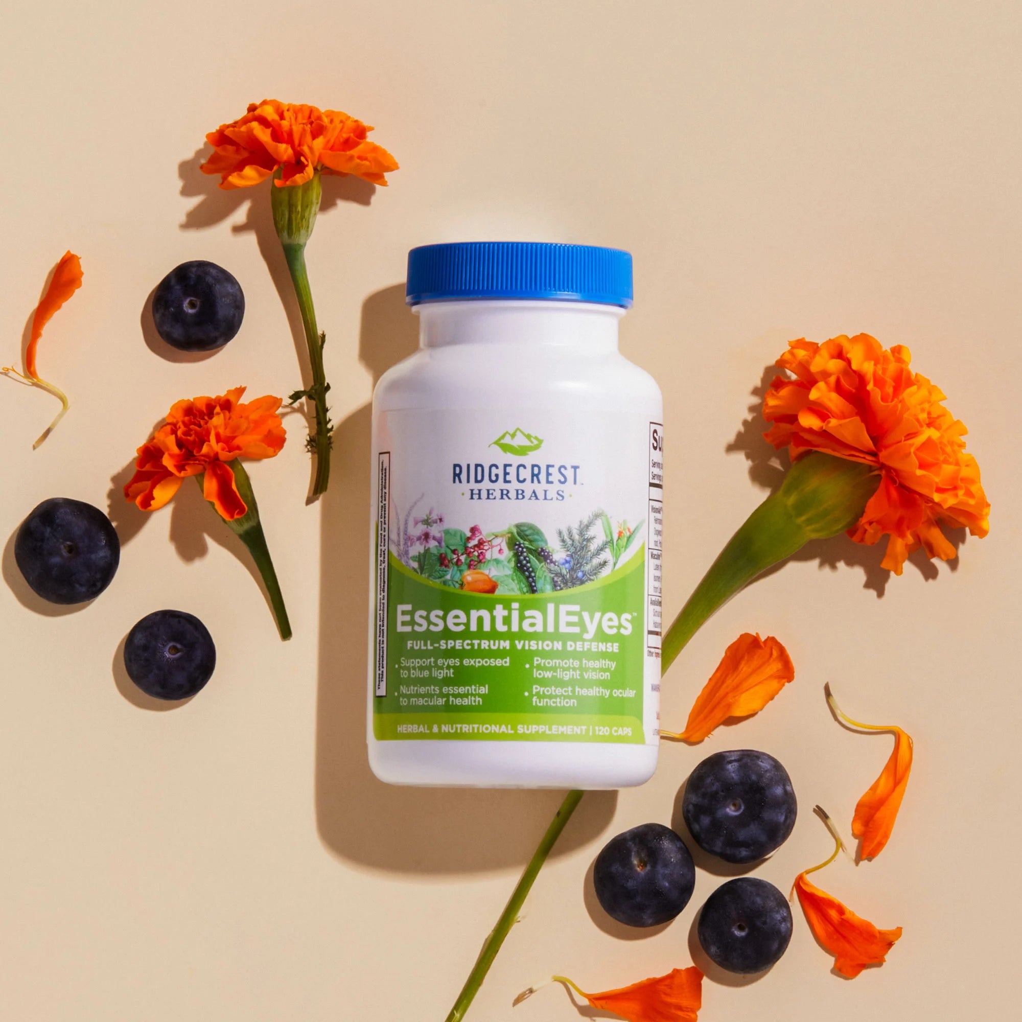 EssentialEyes supplement is displayed with vibrant orange marigold flowers and scattered blueberries, set against a beige background.