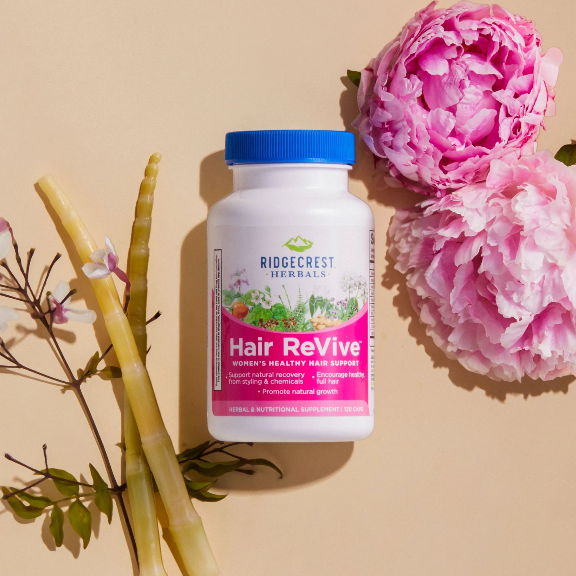 Hair ReVive bottle is displayed with pink peonies, bamboo, and delicate white flowers, set against a beige background.