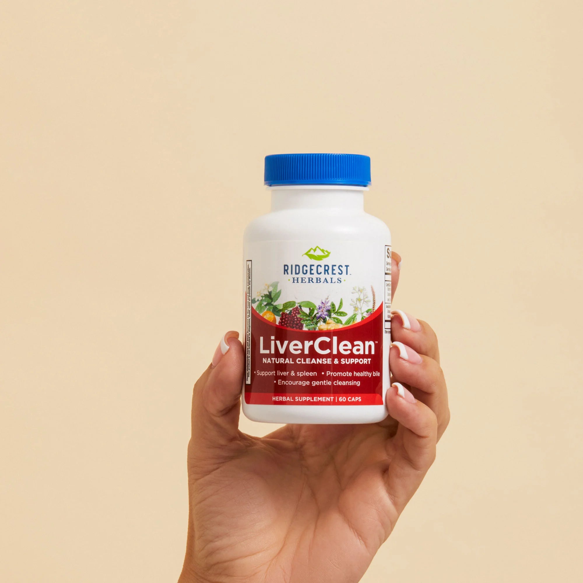 A manicured female hand holds a bottle of LiverClean against a beige background. 