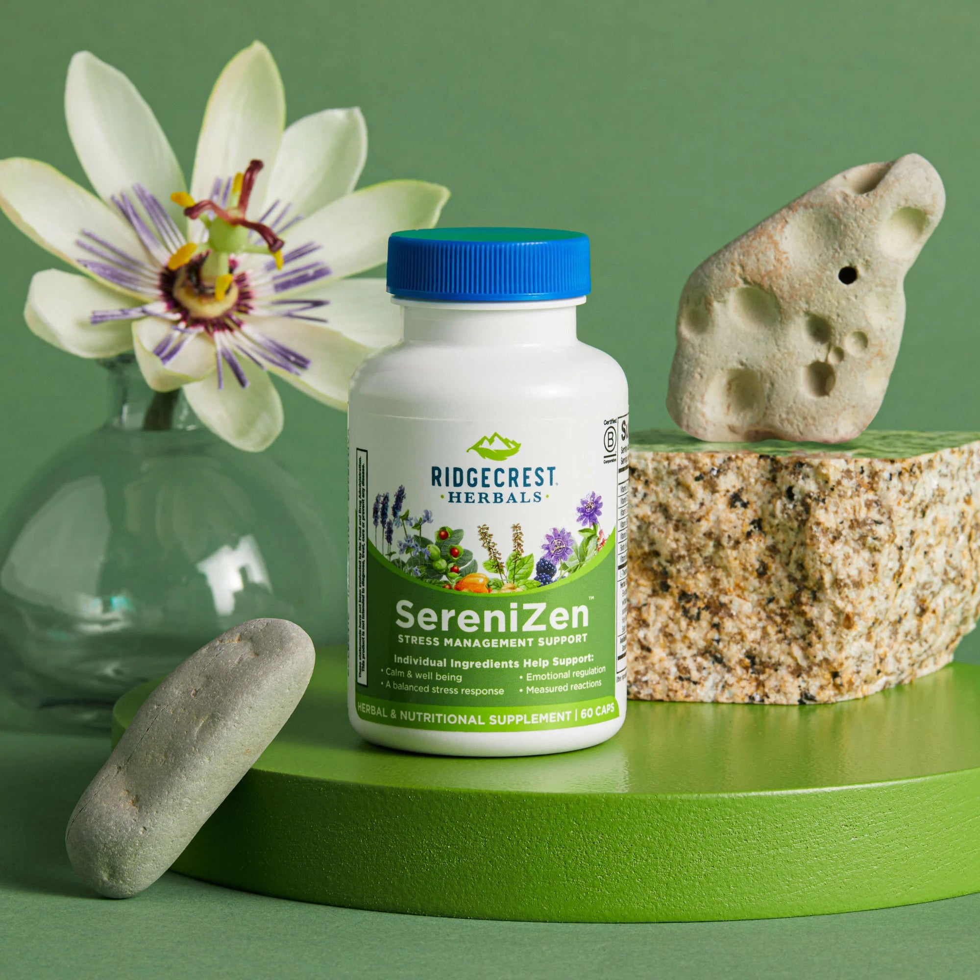 SereniZen sits on a green pedestal with a passionflower in a glass vase and stones on a green background.