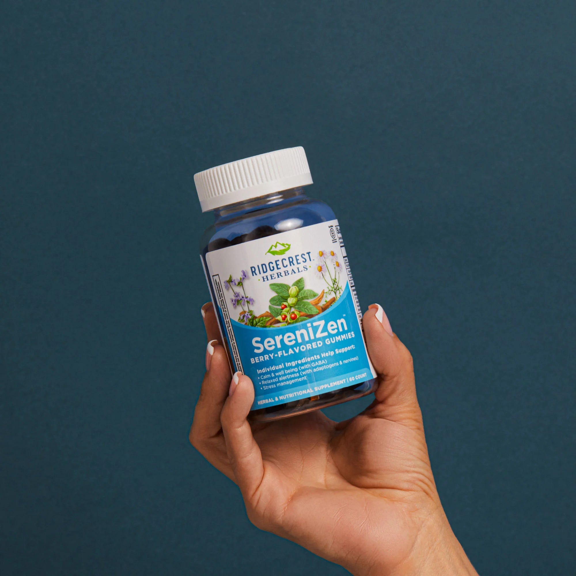 A manicured female hand holds a bottle of SereniZen Gummies against a teal background. 