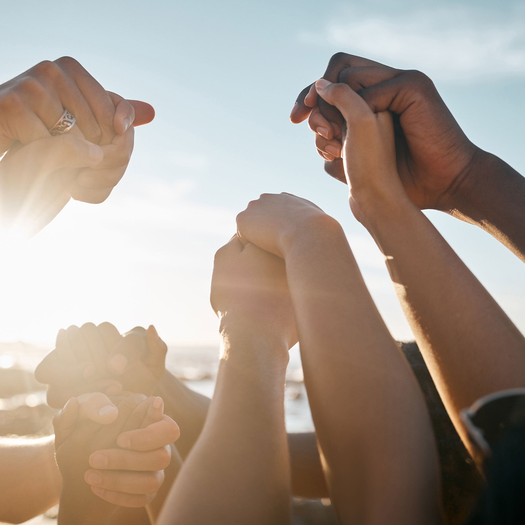 A group of hands of diverse skin tones holding each other tightly, with sunlight shining through, symbolizing unity, strength, and trust